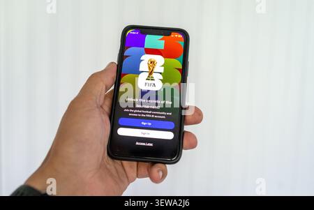 Hand holds smartphone displaying football tournament login screen with colorful graphic background, centered trophy icon, registration buttons, and clean minimal white backdrop for digital engagement. Warsaw, Poland 26-06-2026 Stock Photo
