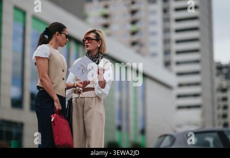 Two businesswomen discussing a report outside a modern office building during an urban meeting Stock Photo