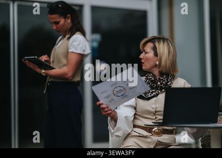 Businesswomen discussing documents and laptop while collaborating outside a modern office building Stock Photo