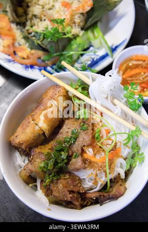Vietnamese grilled pork rice vermicelli bowl with fresh herbs, spring rolls, and dipping sauce. Stock Photo