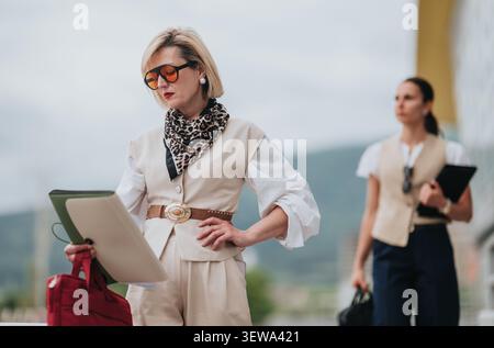 Two professional women working remotely outdoors with laptop and tablet during business travel Stock Photo