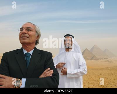 Two confident Middle Eastern businessmen one in dark suit and one in traditional white kandura standing proudly in the Egyptian desert near the Giza Stock Photo