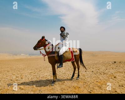 Proud Arab horse rider sitting astride a decorated Arabian horse on the open desert plateau under a hazy sky ideal for equestrian tourism and Stock Photo