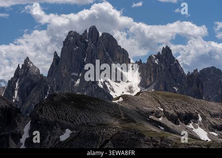 Majestic jagged rocky mountain peaks with patches of white snow under a blue sky with dramatic cumulus clouds, wild alpine landscape and wilderness ex Stock Photo