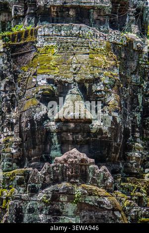 A close-up view of a large, weathered stone face carving, part of the Bayon Temple at Angkor Thom, fills the frame. The carving features prominent eye Stock Photo
