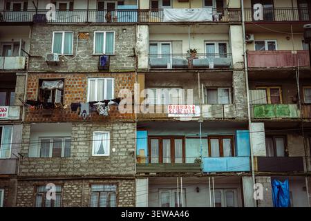 A dense arrangement of apartment building facades, featuring exposed brick, grey concrete blocks, and multiple balconies with various colored railings Stock Photo