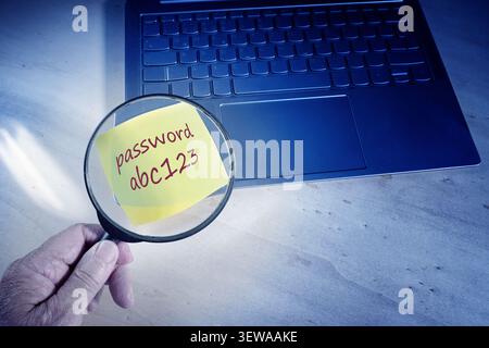 Hand with a magnifying glass finding the insecure password on a sticky note attached to a laptop keyboard, insufficient protection against data theft, Stock Photo