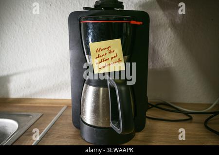 Dirty coffee maker in an old dark kitchen with a sticky note and a reminder, Always place the coffee pot underneath. Dementia or aging forgetfulness i Stock Photo