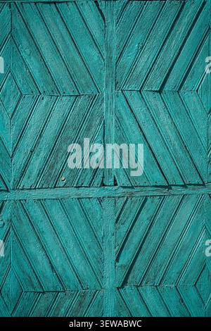 The image shows a close-up, full-frame view of weathered wooden panels painted in a deep teal color. The planks are arranged in a repeating chevron pa Stock Photo