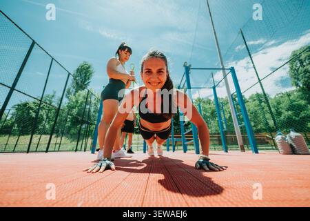 Two women doing push-ups in outdoor fitness training session on a sunny court Stock Photo