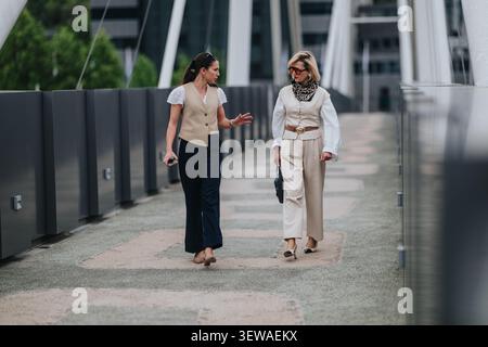 Two businesswomen walking and talking on a modern pedestrian bridge in the city Stock Photo