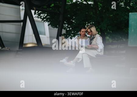Two women reviewing documents while working remotely on a park bench during an outdoor meeting Stock Photo