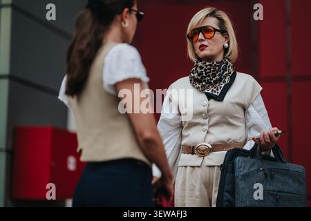 Two businesswomen having a serious conversation outside an office building in fashionable attire Stock Photo