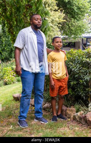 African American father and child posing in yard by shrubs and rock-border, resting hand on child Stock Photo