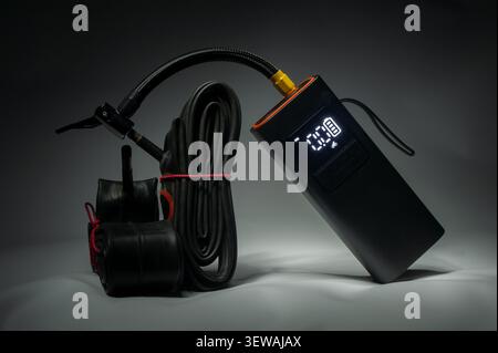 Portable electric tire inflator with digital pressure display, flexible air hose and bicycle tube on dark background, modern air pump for inflating bi Stock Photo