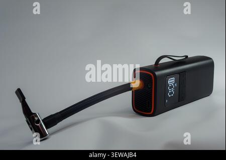 Portable electric tire inflator with digital pressure display, flexible air hose and bicycle tube on dark background, modern air pump for inflating bi Stock Photo
