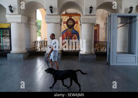 A man walks a black dog through a church with columns and icons in the background. Stock Photo