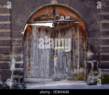 Old wooden door under stone archway. Door shows signs of weathering and decay. Cracked paint and rusted hinges visible Stock Photo