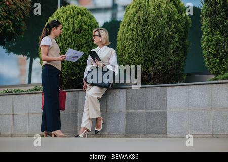 Two businesswomen discussing documents outside office by landscaped planters during a break Stock Photo