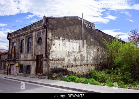 Old, weathered brick building with peeling paint and broken windows. Roof damaged, chimney missing, walls cracked Stock Photo