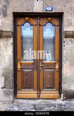 Wooden double door with arched glass panes. Stone wall surrounds the entrance Stock Photo