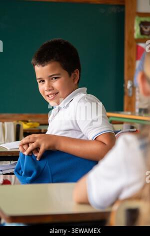 Elementary school boy smiling at classmate in classroom during lesson Stock Photo
