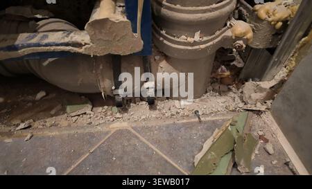 A close-up shot shows old, dusty pipes and construction debris scattered on a dirty tiled floor, likely during a demolition or renovation project. Stock Photo