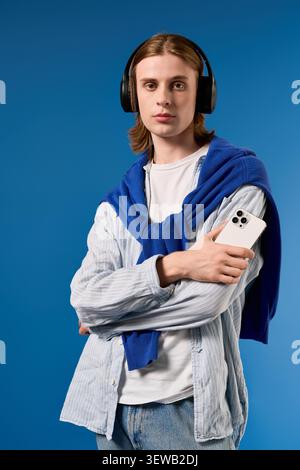 Stylish young man with long hair and headphones, holding a smartphone. Stock Photo