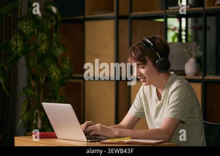 Smiling teen boy learning online with laptop and headphones at home. Stock Photo