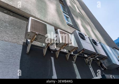 outdoor air conditioner units with rusty brackets mounted on a concrete wall of a high-rise building on a sunny day. Hot weather Stock Photo