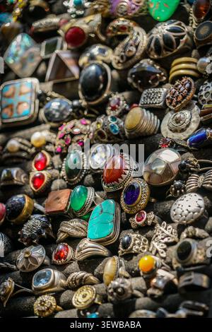 A close-up, high-angle shot captures a dense collection of antique sterling silver rings with various gemstones arranged on a dark, textured display s Stock Photo