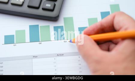 A person pointing a pen at a financial bar chart with a calculator on the side, analyzing quarterly business performance. Shallow depth of field. Clos Stock Photo