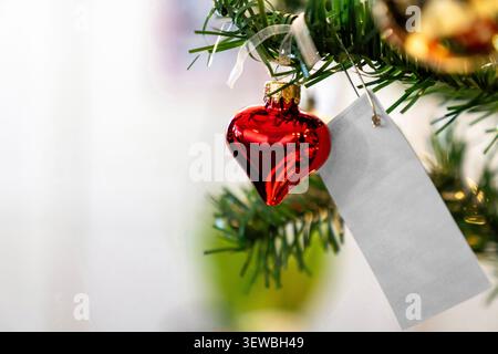 Red heart shaped Christmas tree ornament with a blank white gift tag. Festive holiday decoration for romance and Valentine concepts with copy space. Stock Photo