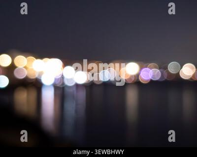 City lights show their colors on the water at night. The blurred circles create a bokeh effect that enhances the beauty of this urban scene by the wat Stock Photo