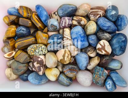 A collection of polished tumbled gemstones is displayed. The stones include blue quartz, tiger's eye, jasper, and amethyst. The vibrant colors create Stock Photo