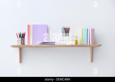 Books, pencils and notebooks on shelf near white wall in child's room Stock Photo