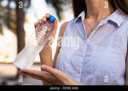 Person holding and drinking from a reusable water bottle in a bright outdoor setting Stock Photo