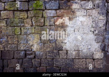 Old stone wall with moss and weathered texture. Dark stones show signs of age and moisture. Surface has patches of lichen and discoloration. Natural p Stock Photo