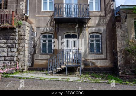 Old stone building with faded paint and metal balcony. Weathered windows, mossy ground, and rusted railings. No visible animals or plants. Graffiti ne Stock Photo
