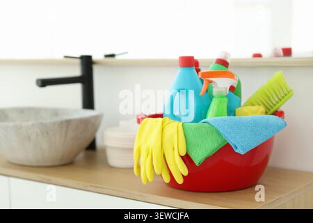 Red plastic basin with cleaning products and supplies on counter in bathroom Stock Photo