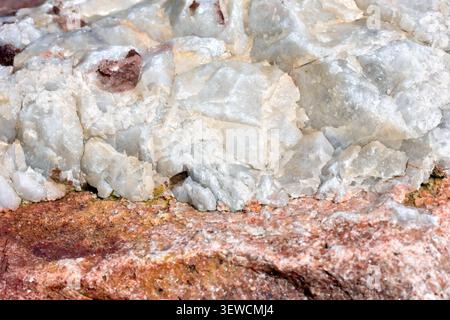 Close up showing detail of a layer of the mineral quartz (silica) embedded across the top of a pink or red boulder, possibly granite. Stock Photo
