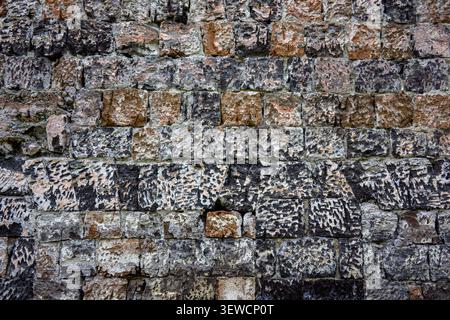 Old stone wall texture with weathered bricks. Crumbling surface shows gray, brown, and white tones. Rough, uneven pattern ideal for backgrounds. Textu Stock Photo