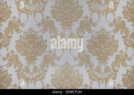 Elegant gold damask motif on a textured cream backdrop, showcasing intricate floral accents, flowing scrollwork, symmetrical baroque-inspired detail Stock Photo