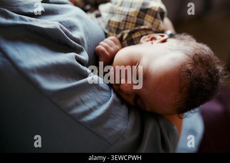 Close up of mother holding sleeping infant against chest, showing caregiving during workday and parenting balance. Ideal for maternity policy, working parent, family support campaigns Stock Photo