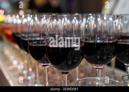 Rows of elegant red wine glasses filled with ruby wine at a tasting. Sophisticated hospitality, fine dining, and winery culture backdrop. Stock Photo