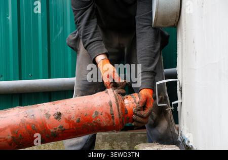 Plumber installing orange plastic sewage pipe outdoor. Worker in gloves fixing sewer pipeline system, drainage installation, construction or Stock Photo