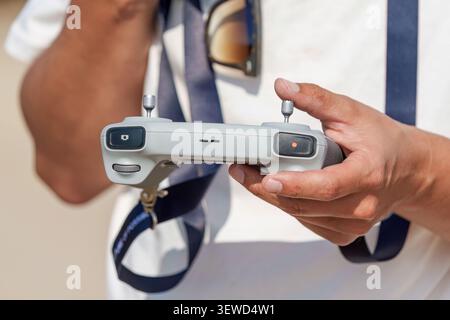 Close-up of a drone pilot holding a remote controller, operating a quadcopter UAV outdoors. Stock Photo