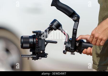 Camera operator holding a mirrorless camera mounted on a professional gimbal stabilizer for video production. Stock Photo