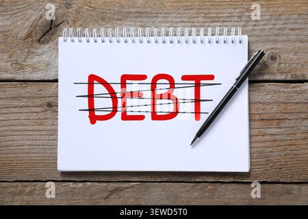 Debt repayment. Notebook with written and crossed out word on wooden table, top view Stock Photo