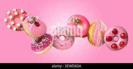 Sweet donuts covered with icing falling on pink background Stock Photo